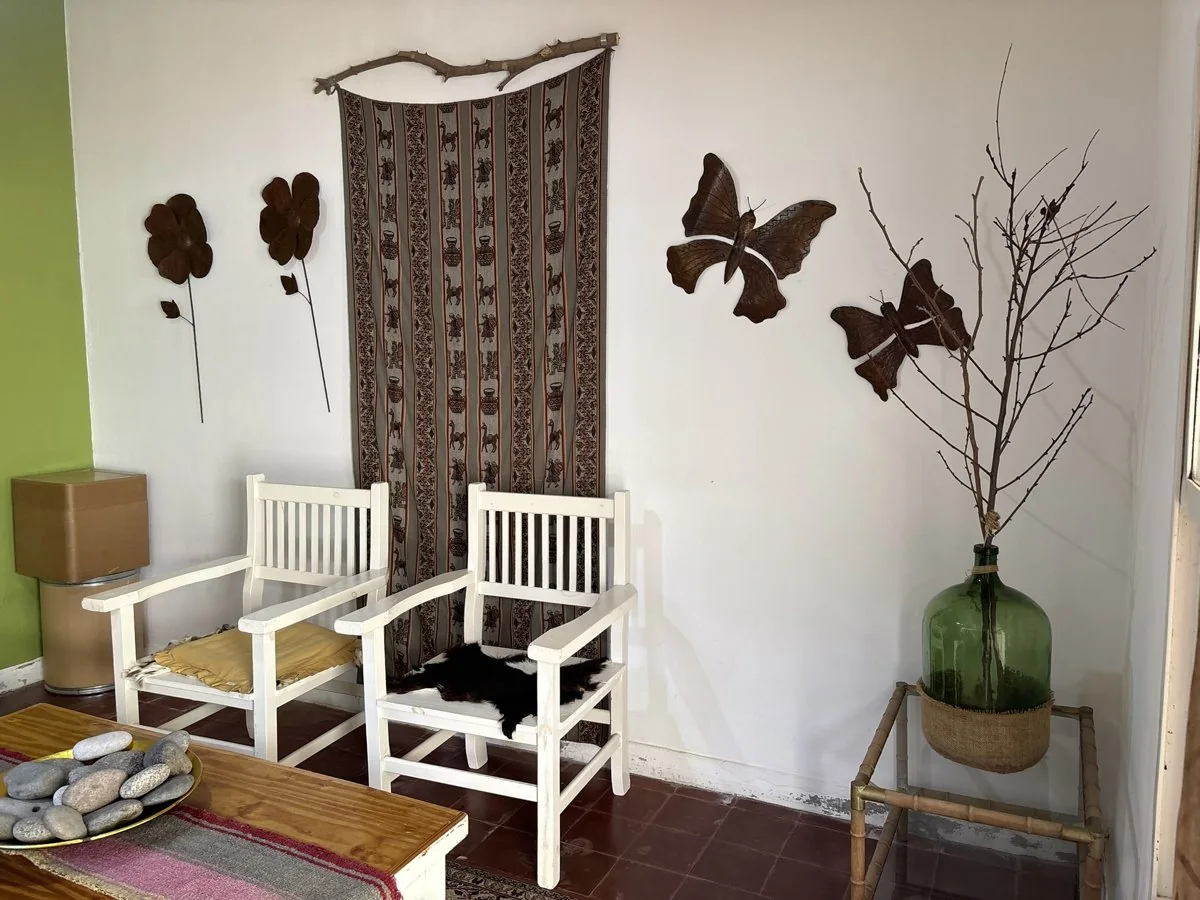 Un estar de la residencia con dos sillas blancas, una mesa de madera y detalles de ambientación.